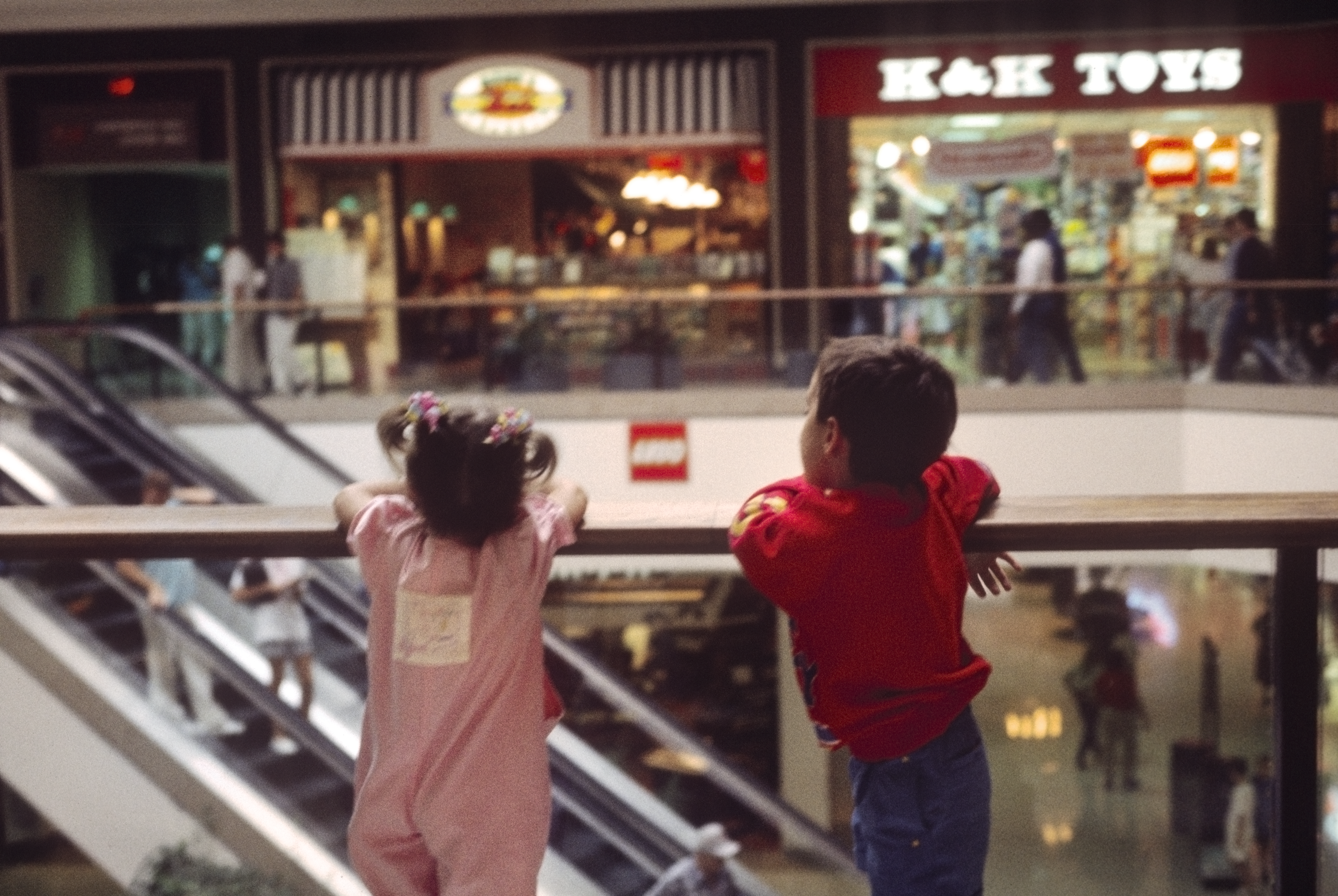A young boy and girl looking over a second floor railing in a mall